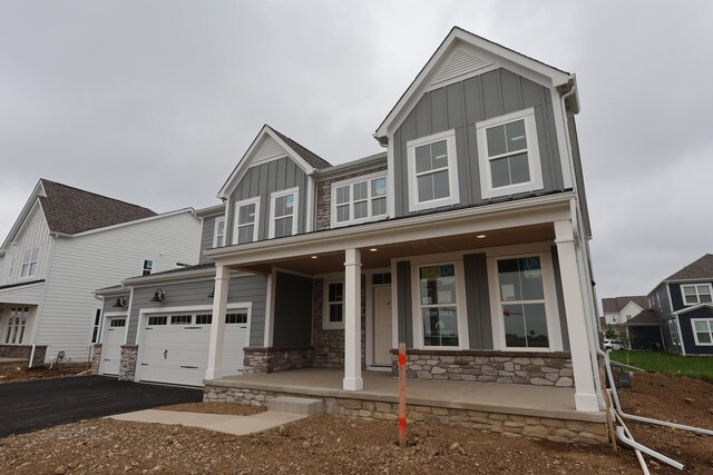 6946 Stillhouse Ln, Dublin, OH 43016 - view of front of home with board and batten siding, a porch, stone siding, asphalt driveway, and an attached garage