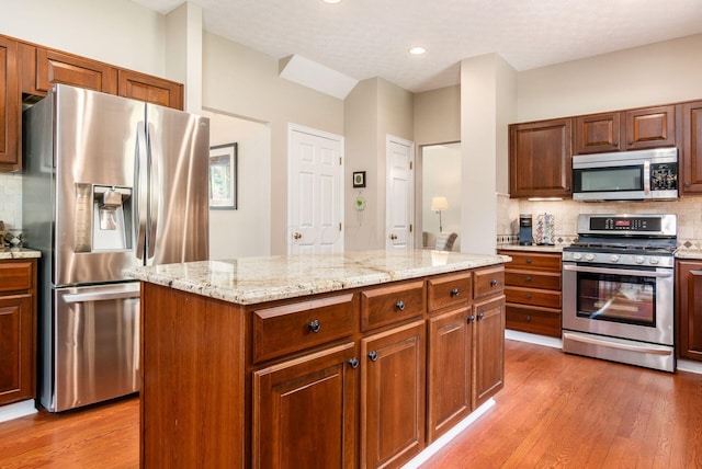 2545 Bryton Dr, Powell, OH 43065 - kitchen featuring stainless steel appliances, light wood finished floors, backsplash, a kitchen island, and light stone counters