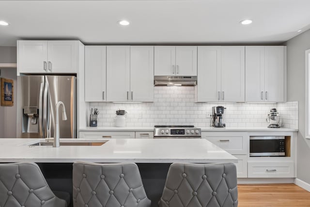 3985 Glenda Pl, Upper Arlington, OH 43220 - kitchen featuring appliances with stainless steel finishes, under cabinet range hood, recessed lighting, a kitchen bar, and decorative backsplash