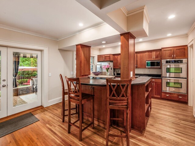 1635 Cambridge Blvd, Upper Arlington, OH 43212 - kitchen featuring stainless steel appliances, dark countertops, ornamental molding, light wood-type flooring, and a kitchen bar