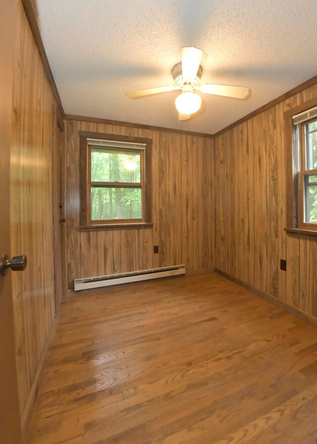 311 Chinook Ln, Sugar Grove, OH 43155 - empty room with a baseboard radiator, a textured ceiling, wood finished floors, wooden walls, and a ceiling fan
