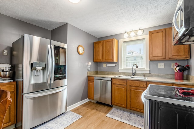 526 N Columbus St, Lancaster, OH 43130 - kitchen with stainless steel appliances, a sink, brown cabinetry, light wood-style floors, and a textured ceiling