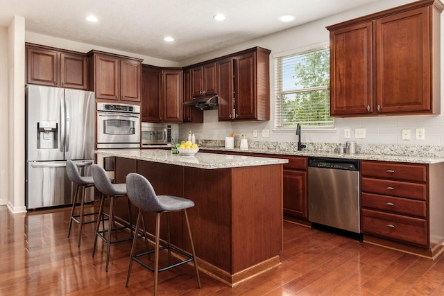 7019 Blakemore Ln, Dublin, OH 43016 - kitchen with stainless steel appliances, dark wood-style flooring, a center island, tasteful backsplash, and a breakfast bar