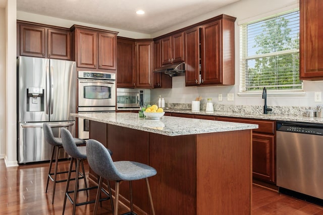 7019 Blakemore Ln, Dublin, OH 43016 - kitchen with stainless steel appliances, dark wood finished floors, a kitchen island, light stone countertops, and a kitchen bar