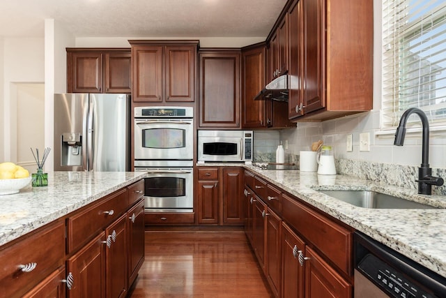 7019 Blakemore Ln, Dublin, OH 43016 - kitchen with appliances with stainless steel finishes, a sink, light stone counters, dark wood finished floors, and decorative backsplash