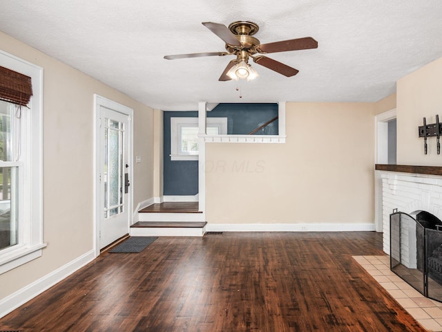 34 Columbus Ave, Delaware, OH 43015 - unfurnished living room featuring wood finished floors, healthy amount of natural light, baseboards, a brick fireplace, and a textured ceiling