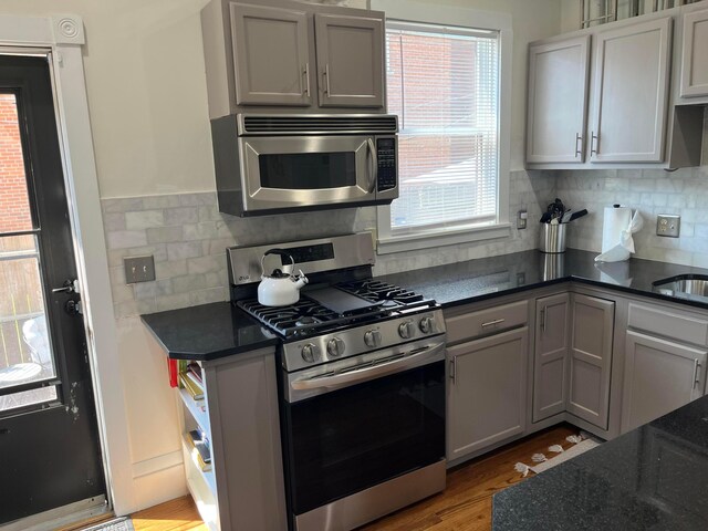 323 E Kossuth St, Columbus, OH 43206 - kitchen featuring stainless steel appliances, backsplash, gray cabinets, light wood-style flooring, and dark stone countertops