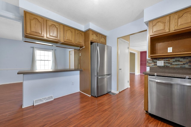 883 Mcnaughten Rd, Columbus, OH 43213 - kitchen with appliances with stainless steel finishes, dark countertops, dark wood finished floors, decorative backsplash, and brown cabinetry