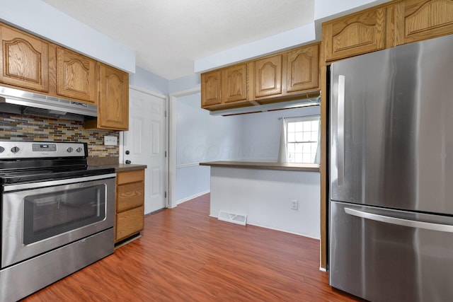 883 Mcnaughten Rd, Columbus, OH 43213 - kitchen featuring stainless steel appliances, under cabinet range hood, dark wood-style floors, backsplash, and brown cabinets