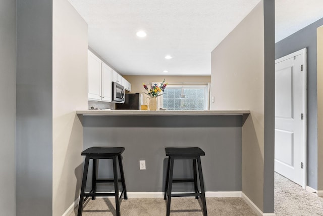 5290 Berthold Pass Dr, Dublin, OH 43016 - kitchen featuring stainless steel microwave, white cabinetry, a kitchen breakfast bar, light colored carpet, and a peninsula