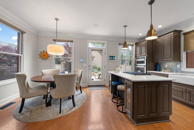 1054 Perry St, Columbus, OH 43201 - kitchen with light countertops, stainless steel appliances, dark brown cabinets, a center island, and ornamental molding