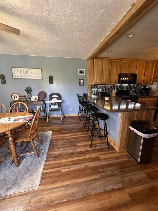 4902 Columbus Sandusky Rd N, Marion, OH 43302 - kitchen featuring a textured ceiling, black electric range, wood finished floors, backsplash, and a kitchen breakfast bar