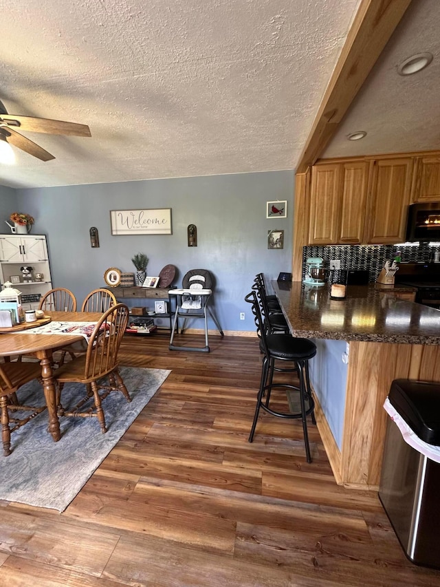 4902 Columbus Sandusky Rd N, Marion, OH 43302 - kitchen with a textured ceiling, ceiling fan, dark wood finished floors, a breakfast bar, and decorative backsplash