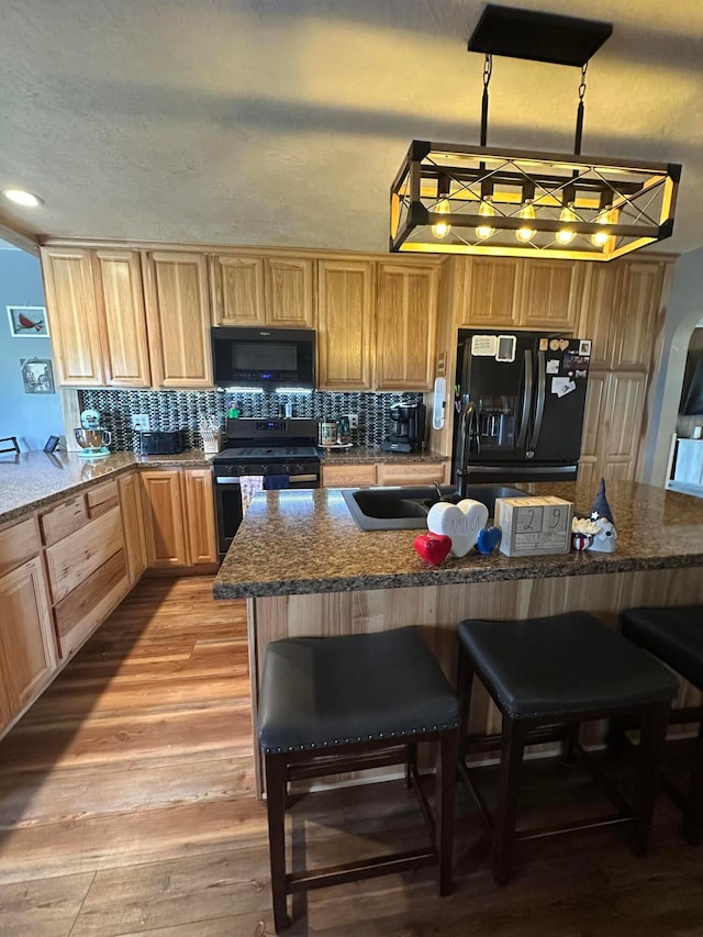 4902 Columbus Sandusky Rd N, Marion, OH 43302 - kitchen with black appliances, a sink, light wood-type flooring, a breakfast bar, and tasteful backsplash