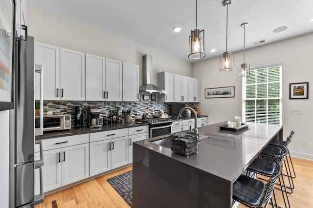 233 S Ohio Ave Unit 11, Columbus, OH 43205 - kitchen with wall chimney exhaust hood, stainless steel appliances, tasteful backsplash, light wood-type flooring, and a breakfast bar