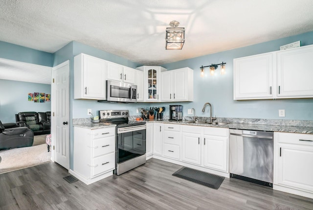 3097 Lee Ellen Pl, Columbus, OH 43207 - kitchen featuring stainless steel appliances, a sink, wood finished floors, light stone counters, and a textured ceiling