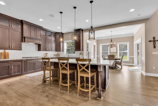9568 Craigens Ct, Galena, OH 43021 - kitchen with decorative backsplash, a kitchen island, gas stovetop, light wood-type flooring, and a breakfast bar area
