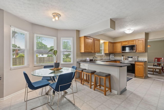 6897 Roundelay Rd N, Reynoldsburg, OH 43068 - kitchen featuring stainless steel appliances, a peninsula, dark countertops, a breakfast bar, and baseboards