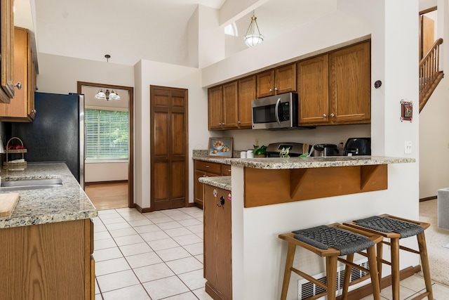 5839 Castleknock Rd, Dublin, OH 43016 - kitchen featuring stainless steel microwave, a sink, a peninsula, brown cabinets, and a breakfast bar area