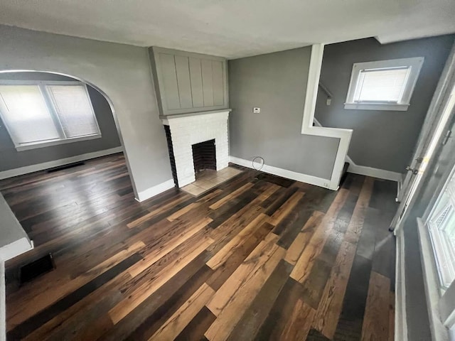 1403 Genessee Ave, Columbus, OH 43211 - unfurnished living room featuring dark wood finished floors, baseboards, a fireplace, arched walkways, and stairs