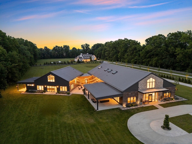 3226 Bean Oller Rd, Delaware, OH 43015 - back of house at dusk with curved driveway, stone siding, and a lawn