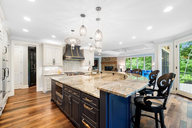 5633 Travis Pointe Ct, Westerville, OH 43082 - kitchen with custom exhaust hood, white cabinetry, recessed lighting, tasteful backsplash, and a kitchen bar