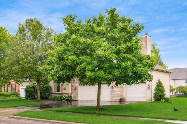 7985 Eric Ct, Lewis Center, OH 43035 - obstructed view of property with a front yard, concrete driveway, stucco siding, stone siding, and a chimney