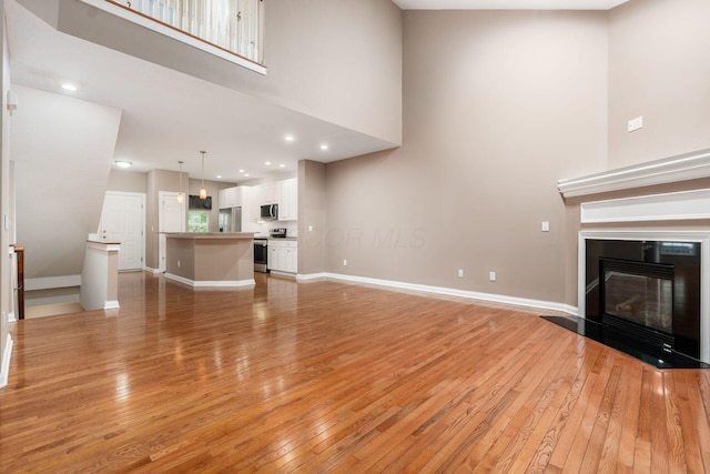 6618 Wild Rose Ln, Westerville, OH 43082 - unfurnished living room with light wood-type flooring, a towering ceiling, a glass covered fireplace, and baseboards