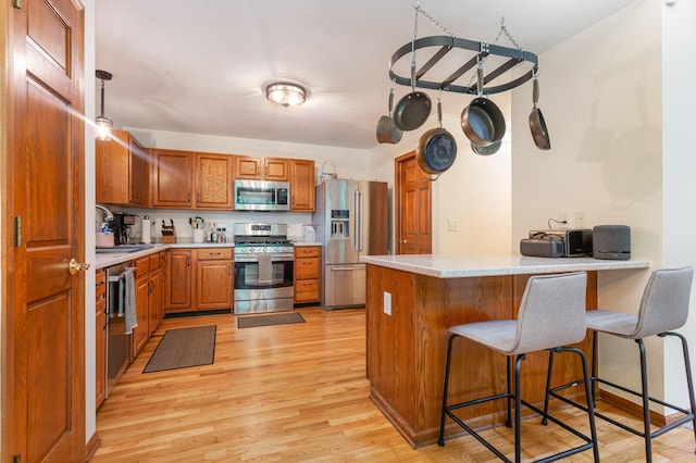 1315 Shelby Cir, Reynoldsburg, OH 43068 - kitchen featuring appliances with stainless steel finishes, a peninsula, brown cabinetry, light wood-style floors, and light countertops