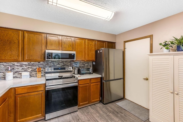 7179 Inverness Ct, Dublin, OH 43016 - kitchen featuring stainless steel appliances, light countertops, light wood finished floors, decorative backsplash, and brown cabinetry