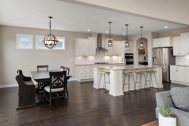 3669 Audubon Ave, Hilliard, OH 43026 - kitchen with wall chimney exhaust hood, appliances with stainless steel finishes, decorative backsplash, a breakfast bar, and a center island with sink