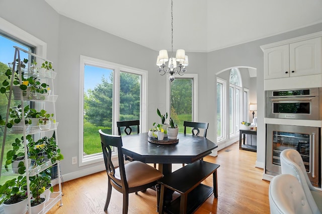 9146 Shawnee Trl, Powell, OH 43065 - dining area featuring arched walkways, wine cooler, a chandelier, light wood-type flooring, and a towering ceiling