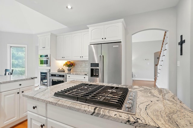 9146 Shawnee Trl, Powell, OH 43065 - kitchen with stainless steel appliances, light stone counters, arched walkways, decorative backsplash, and white cabinets