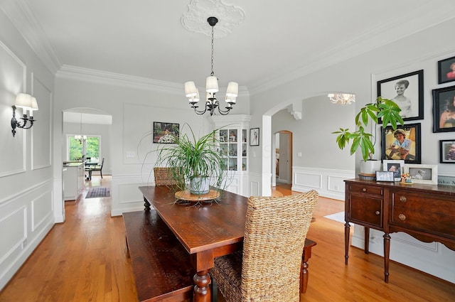 9146 Shawnee Trl, Powell, OH 43065 - dining space with a chandelier, arched walkways, crown molding, light wood-style flooring, and a decorative wall