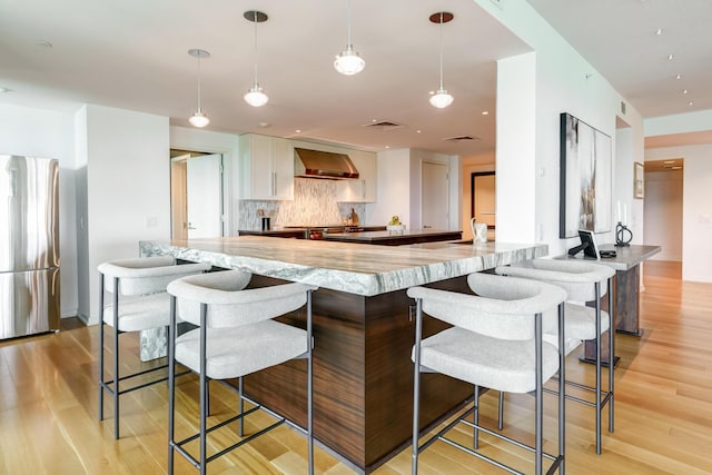 1 Miranova Pl Unit 1225, Columbus, OH 43215 - kitchen featuring freestanding refrigerator, wall chimney exhaust hood, light wood-style flooring, and tasteful backsplash