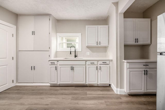960 Carpenter St, Columbus, OH 43206 - kitchen with a sink, a textured ceiling, light countertops, white cabinets, and light wood-type flooring