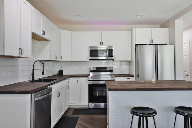1208 Seymour Ave, Columbus, OH 43206 - kitchen with wood counters, appliances with stainless steel finishes, a sink, a kitchen breakfast bar, and white cabinets
