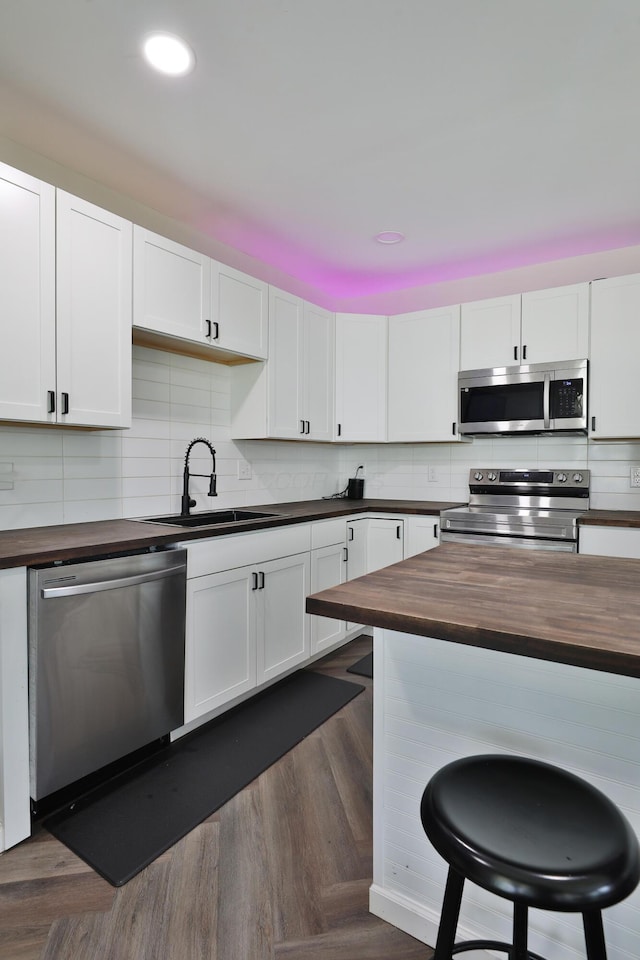 1208 Seymour Ave, Columbus, OH 43206 - kitchen with appliances with stainless steel finishes, butcher block countertops, a sink, a breakfast bar area, and decorative backsplash
