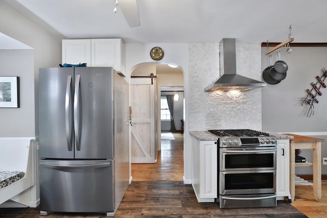 155 Aldrich Rd, Columbus, OH 43214 - kitchen featuring appliances with stainless steel finishes, wall chimney range hood, a barn door, arched walkways, and white cabinetry
