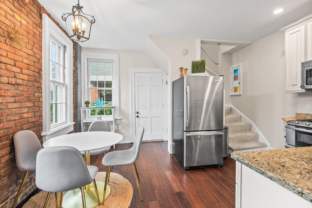 145 E Sycamore St, Columbus, OH 43206 - kitchen with appliances with stainless steel finishes, dark wood-style flooring, brick wall, a chandelier, and white cabinets