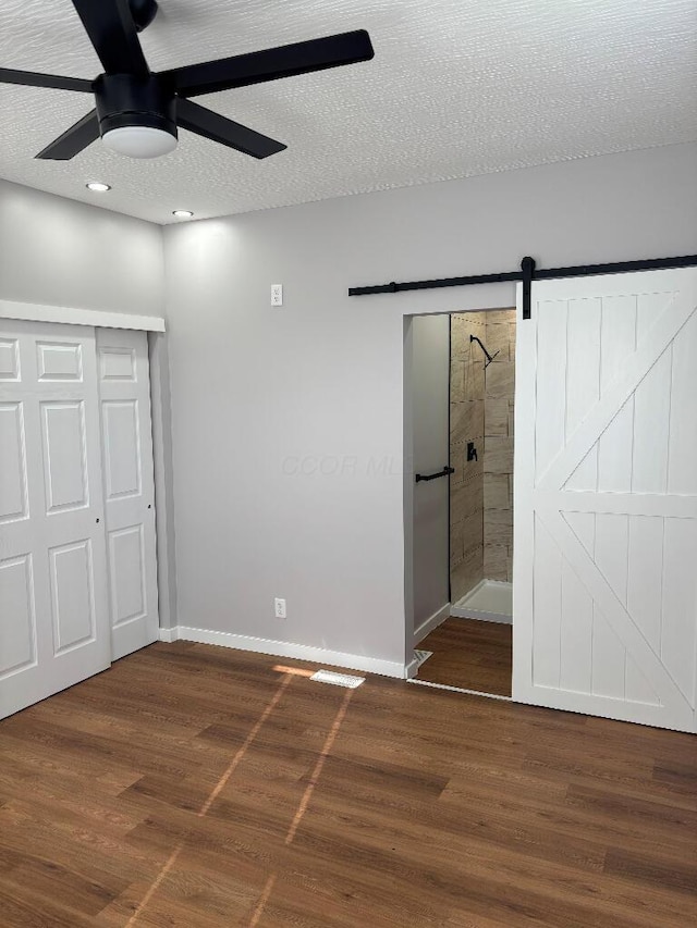 418 Clinton St, Circleville, OH 43113 - unfurnished bedroom with a barn door, wood finished floors, baseboards, a ceiling fan, and a textured ceiling
