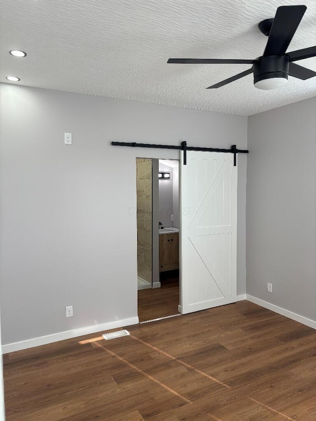 418 Clinton St, Circleville, OH 43113 - unfurnished bedroom with a barn door, wood finished floors, baseboards, ensuite bath, and a textured ceiling