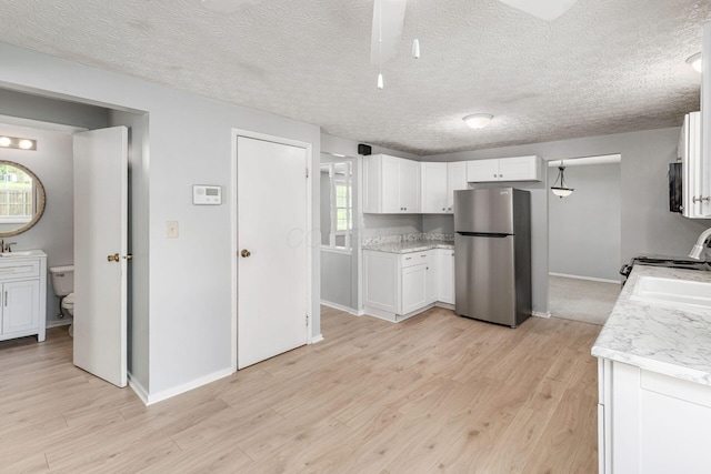 6541 Skywae Dr, Columbus, OH 43229 - kitchen with freestanding refrigerator, light wood-style floors, white cabinetry, healthy amount of natural light, and a textured ceiling