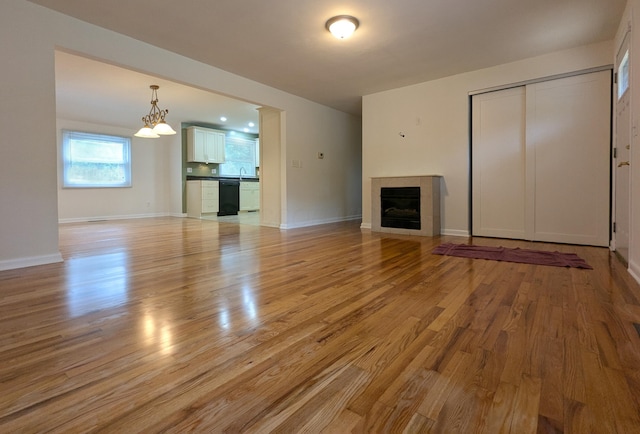 1134 Garden Rd, Columbus, OH 43224 - unfurnished living room with light wood finished floors, a fireplace, a chandelier, baseboards, and a sink