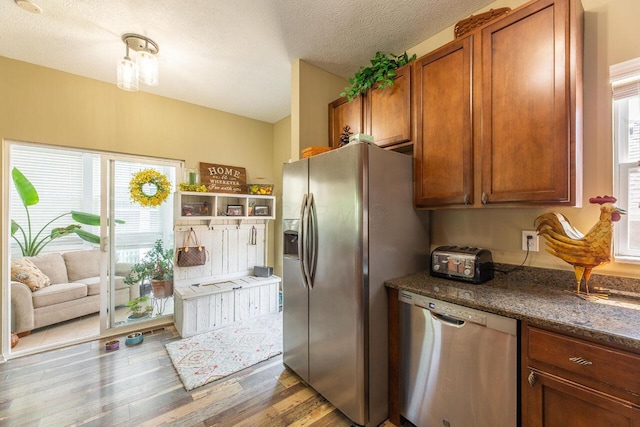 183 W Case St, Powell, OH 43065 - kitchen featuring stainless steel appliances, brown cabinets, light wood-style flooring, dark stone countertops, and a textured ceiling