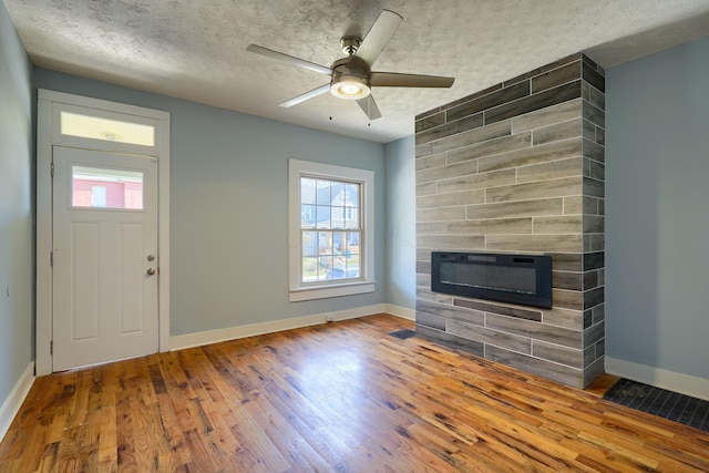909-915 Wilson Ave, Columbus, OH 43206 - unfurnished living room featuring a tiled fireplace, baseboards, wood finished floors, plenty of natural light, and a textured ceiling