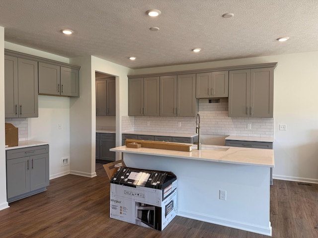 3323 Tender Ave Lot 7165, Powell, OH 43065 - kitchen featuring gray cabinetry, backsplash, dark wood-style flooring, a center island with sink, and a textured ceiling