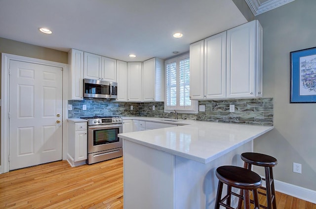 651 S 6th St, Columbus, OH 43206 - kitchen with appliances with stainless steel finishes, a peninsula, a breakfast bar, light wood-type flooring, and white cabinetry