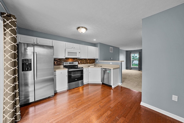 5801 Bridgehampton Dr, New Albany, OH 43054 - kitchen featuring appliances with stainless steel finishes, a peninsula, light countertops, white cabinets, and wood finished floors