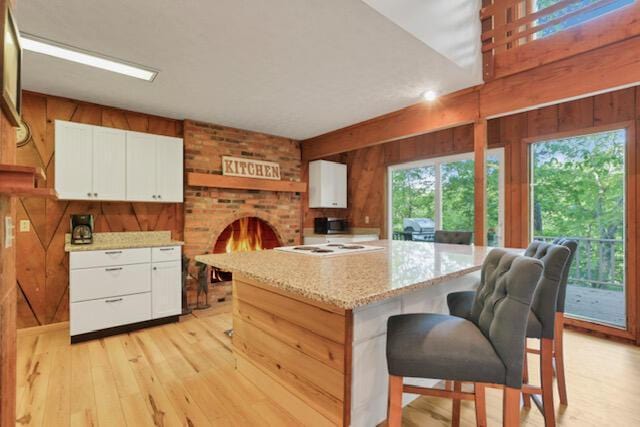 1275 Taos Ln, Sugar Grove, OH 43155 - kitchen featuring wood walls, light wood-style flooring, white cabinetry, a kitchen island, and light stone counters